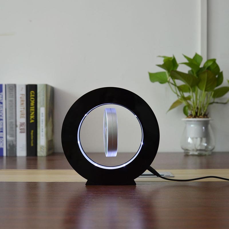 Black magnetic levitation miniature photo frame with LED lights floating on wooden table with books and plant in background