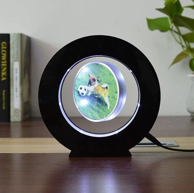 Black magnetic levitation miniature photo frame with LED lights displaying a floating round photo of a dog with a soccer ball on a wooden surface.